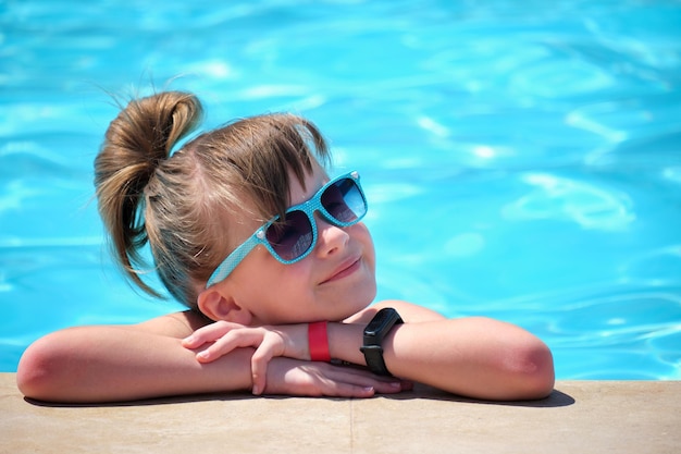 Retrato de una niña feliz relajándose al lado de la piscina en un día soleado de verano durante las vacaciones tropicales