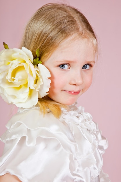 Retrato de una niña feliz con una rosa en el pelo en rosa