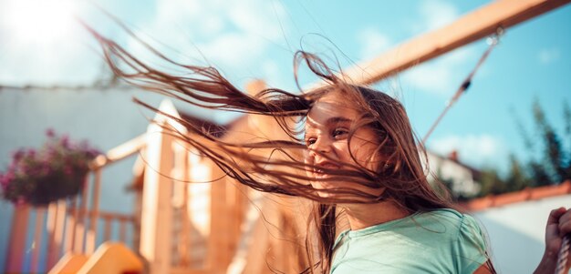 Foto retrato de una niña feliz sentada en un columpio con el pelo largo volando