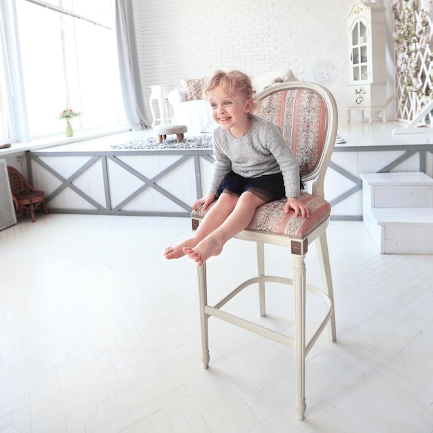 Retrato de niña feliz sentada en una silla en el espacioso