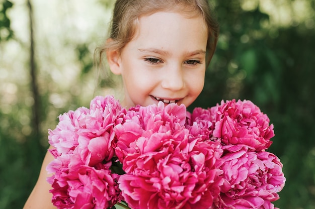 Retrato de una niña feliz sosteniendo un ramo de flores de peonía rosa en flor