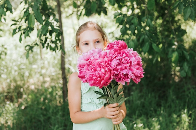 Retrato de una niña feliz sostiene en sus manos un ramo de flores de peonía rosa en plena floración