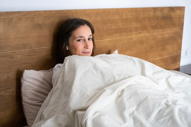 retrato de una niña feliz en su cama cubriéndose con la sábana