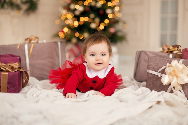 Retrato de niña feliz en suéter de punto rojo con caja de regalo de Navidad cerca del árbol de Navidad.