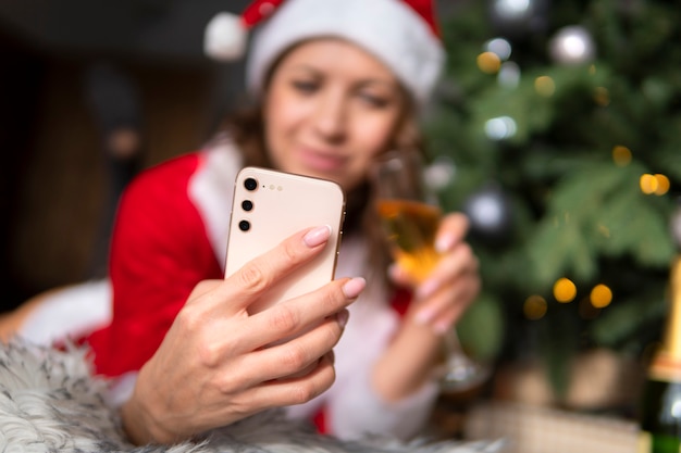 Retrato de niña feliz con teléfono durante la celebración de la Navidad en casa. mujer joven en un traje de Santa Claus es fotografiada en un teléfono inteligente.