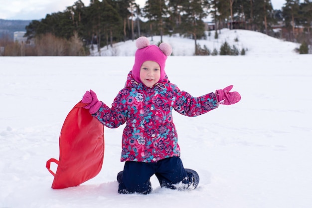 Retrato de una niña feliz con un trineo en la nieve contra una colina.