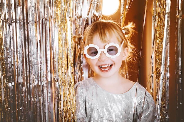 Retrato de niña feliz en vestido y gafas de sol divirtiéndose en el fondo festivo