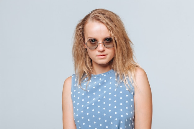 Retrato de una niña con gafas redondas y un vestido azul sobre un fondo gris claro