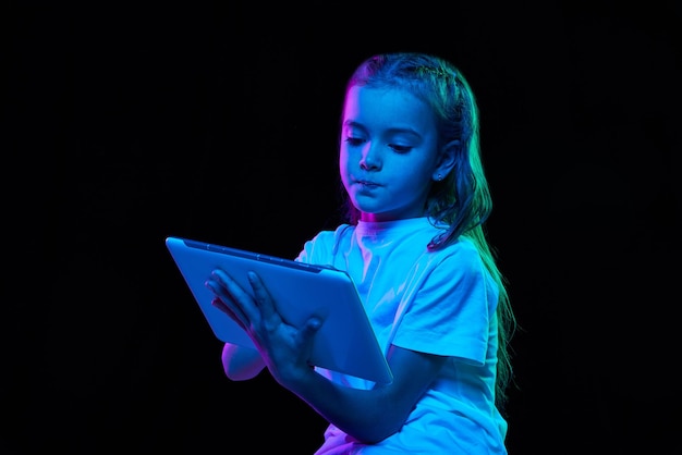 Retrato de niña hermosa en camiseta blanca posando con tableta aislada sobre negro