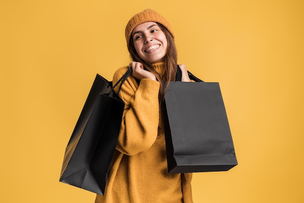 Retrato de niña hermosa emocionada con ropa casual sosteniendo bolsas de compras aisladas sobre fondo amarillo. Concepto de viernes negro