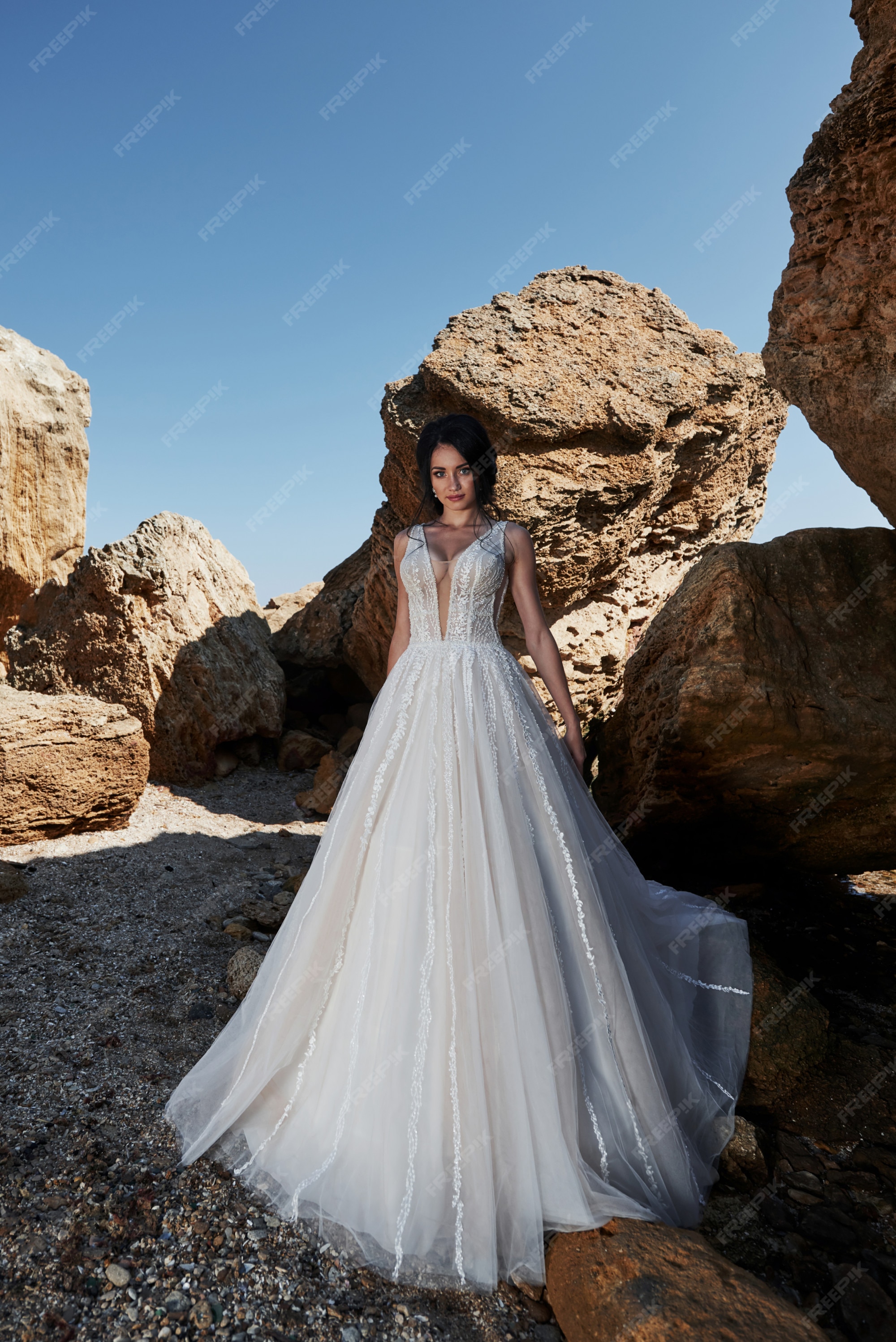 Retrato de una niña en un hermoso vestido de novia posando a un fotógrafo en playa. la novia está las rocas | Foto