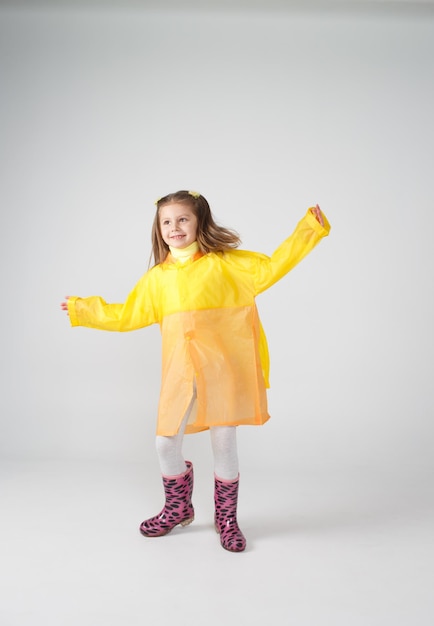 Retrato de una niña con un impermeable amarillo y botas sobre un fondo blanco aislado.