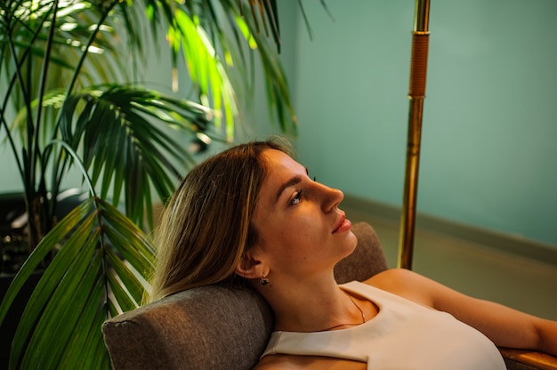 Foto retrato de una niña impresionante sentado en una silla cerca de la planta