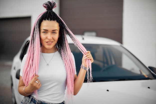 Retrato de una niña independiente con coletas rosadas en el fondo del cielo y el automóvil.