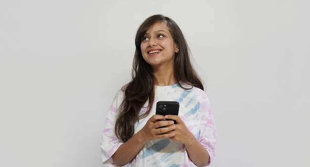 Foto retrato de una niña india sosteniendo un teléfono inteligente y enviando mensajes de texto en el estudio sobre un fondo gris