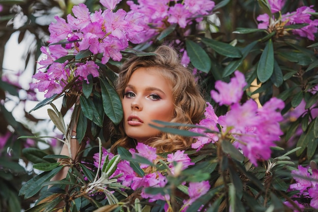 Retrato de una niña en un jardín floreciente Un arbusto de flores es rosa rododendro Hermoso cabello y maquillaje