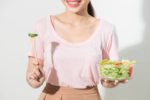 Retrato de una niña juguetona feliz comiendo ensalada fresca de un tazón y guiñando un ojo aislado