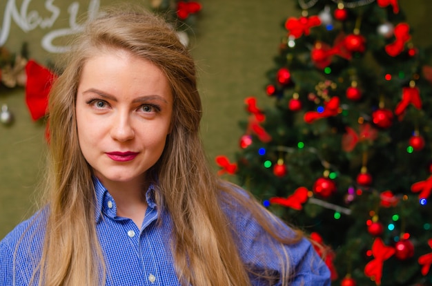 Retrato de una niña con labios rojos brillantes, cabello largo rubio Niña en una camisa de hombre azul. Días festivos. Feliz Navidad. cara graciosa