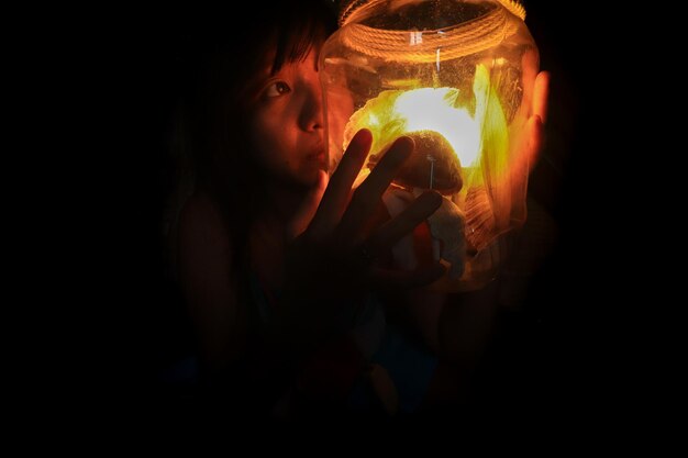 Foto retrato de una niña con una lámpara en la oscuridad