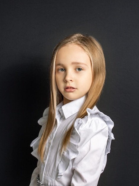 Retrato de niña linda con cabello rubio aislado sobre fondo negro