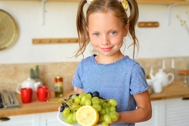 Retrato de una niña linda en la cocina con abarrotes y comida sana