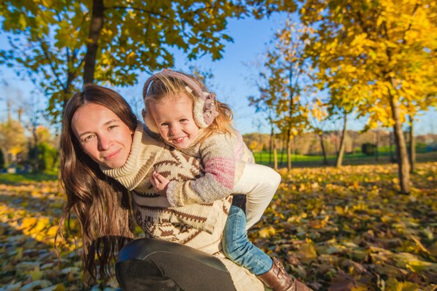 Retrato de niña linda y feliz madre divertirse en el bosque amarillo del otoño en un cálido día soleado