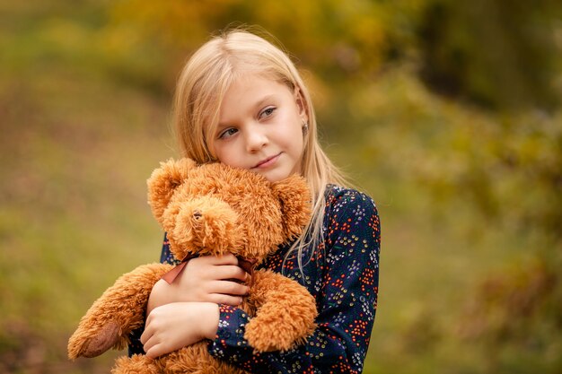 Retrato de una niña linda feliz en el parque otoño con un cachorro de oso de juguete en sus manos