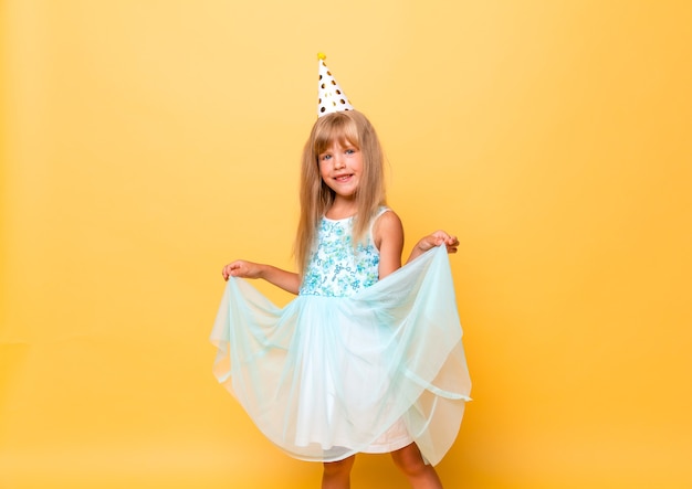 Retrato de una niña linda con un gorro festivo y con globos sobre un fondo amarillo.