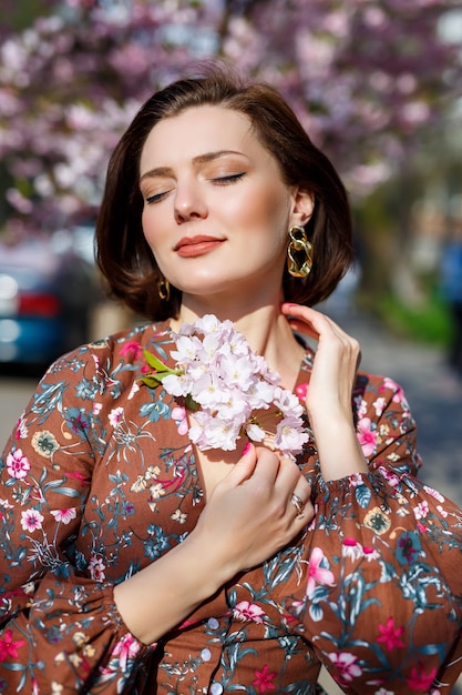 Retrato de una niña linda y hermosa mujer con un vestido en el jardín en medio de la flor de sakura. primavera y sol. Fondo borroso y foco seleccionado.