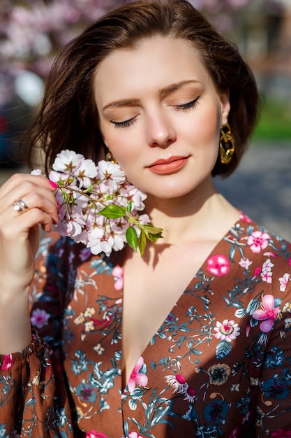 Retrato de una niña linda y hermosa mujer con un vestido en el jardín en medio de la flor de sakura. primavera y sol. Fondo borroso y foco seleccionado.