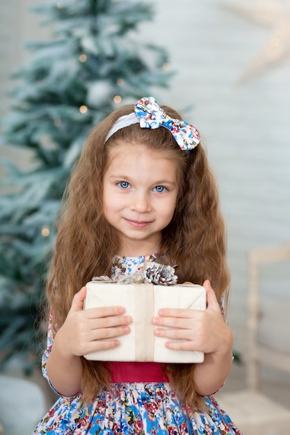 Retrato de una niña linda en un hermoso vestido sonriente sosteniendo una caja con un regalo de Navidad en sus manos