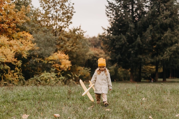 Retrato de una niña linda jugando con un avión de juguete amarillo en el parque de otoño niña molesta jugando y caminando sola