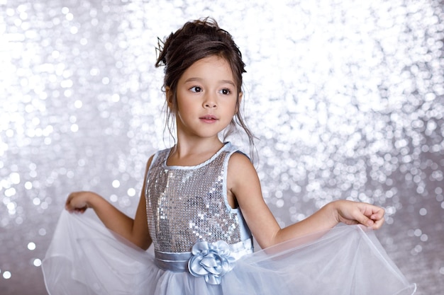 Retrato de niña linda niña sonriente en vestido de princesa sobre fondo con bokeh plateado. fiesta de cumpleaños