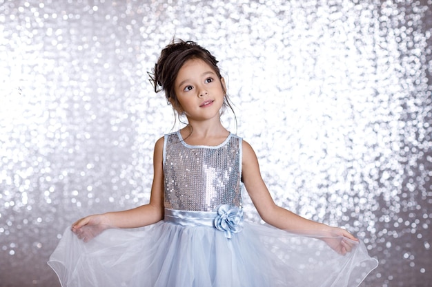 Retrato de niña linda niña sonriente en vestido de princesa sobre fondo con bokeh plateado. fiesta de cumpleaños