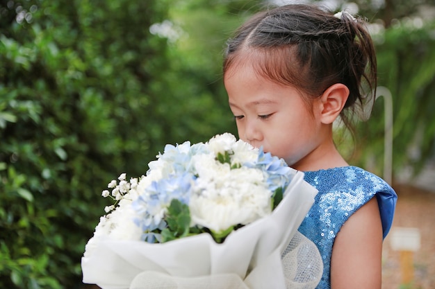 Retrato de la niña linda del niño que huele el ramo de flores en el jardín.