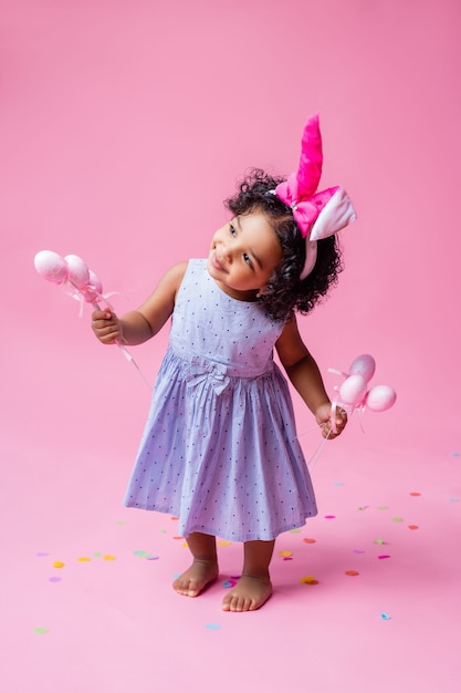 retrato de una niña linda con orejas de conejo de Pascua en la cabeza con huevos de Pascua. estudio, fondo rosa