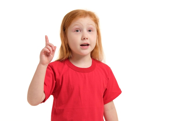 Retrato de niña linda pelirroja emocional con el dedo hacia arriba aislado en un blanco