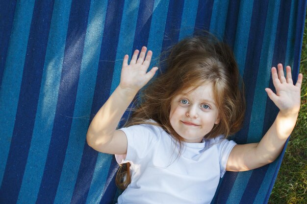 Retrato de una niña linda con el pelo largo descansando en una hamaca en el jardín y sonriendo