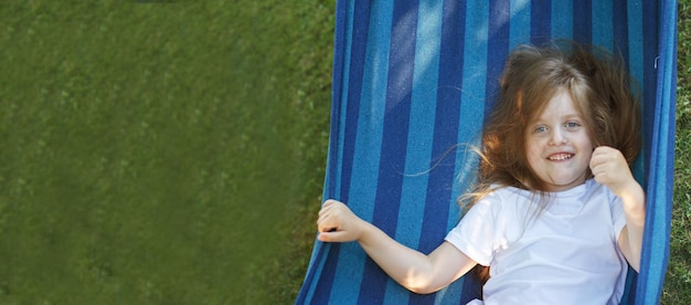 Retrato de una niña linda con el pelo largo descansando en una hamaca en el jardín y sonriendo