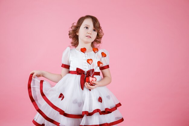 Retrato de niña linda de pie en vestido blanco con donas o corazón de cristal en rosa en el estudio