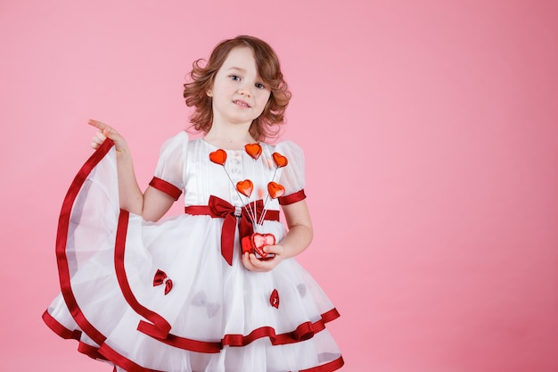 Retrato de niña linda de pie en vestido blanco con donas o corazón de cristal en rosa en el estudio