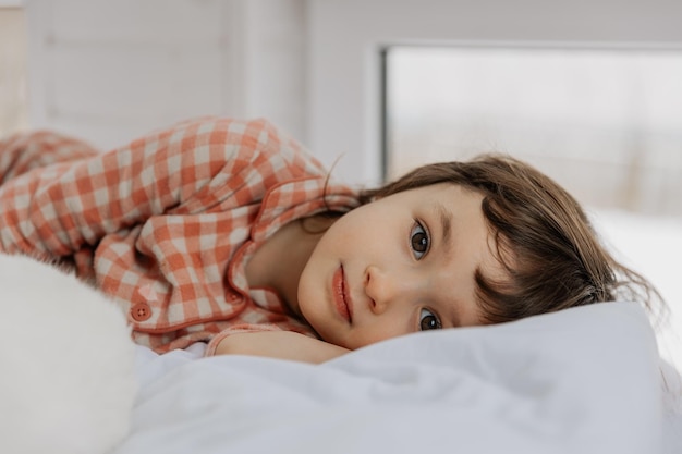 retrato de una niña linda en pijama acostada en una almohada y mirando hacia el marco