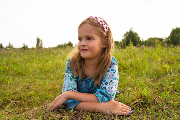 Retrato de una niña linda en un prado. Hermosa niña de 7-9 años con cabello castaño rizado.