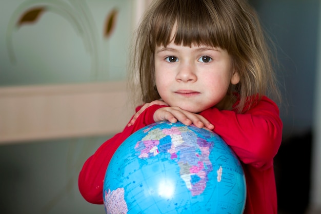 Retrato de la niña linda que abraza el globo de la tierra.