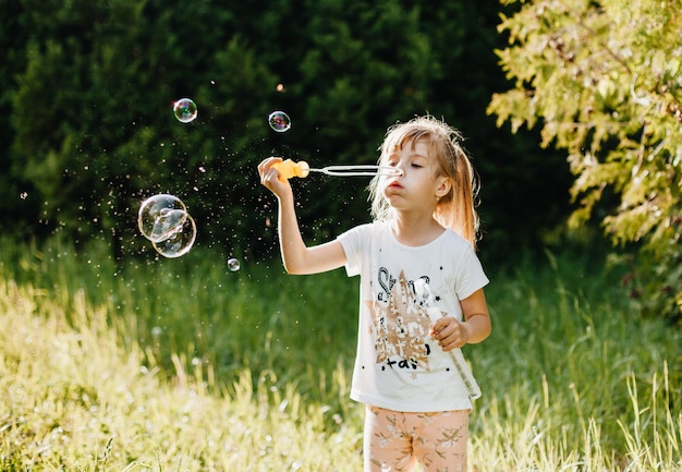 Retrato de una niña linda que sopla pompas de jabón en el parque en verano