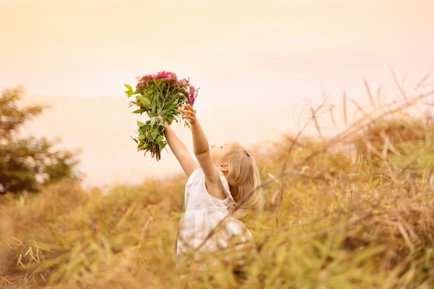 Retrato de la niña linda que sostiene el ramo de las manos de flores rosadas en un campo