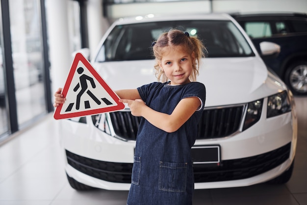 Retrato de niña linda que tiene señal de tráfico en las manos en el salón del automóvil.