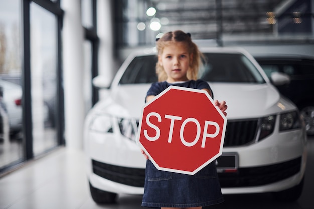 Retrato de niña linda que tiene señal de tráfico en las manos en el salón del automóvil.