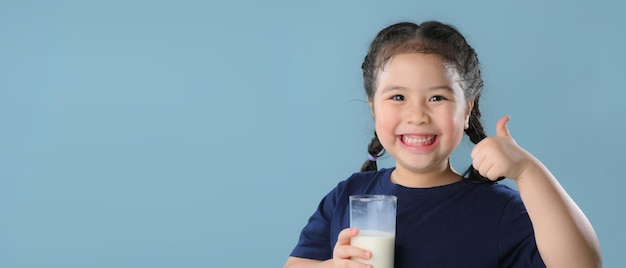 Retrato de una niña linda satisfecha con un vaso de leche aislado sobre fondo azul.