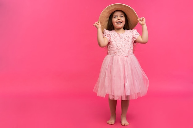 Retrato de niña linda con sombrero de paja y vestido rosa en el estudio sobre fondo rosa. Copie el espacio para el texto.